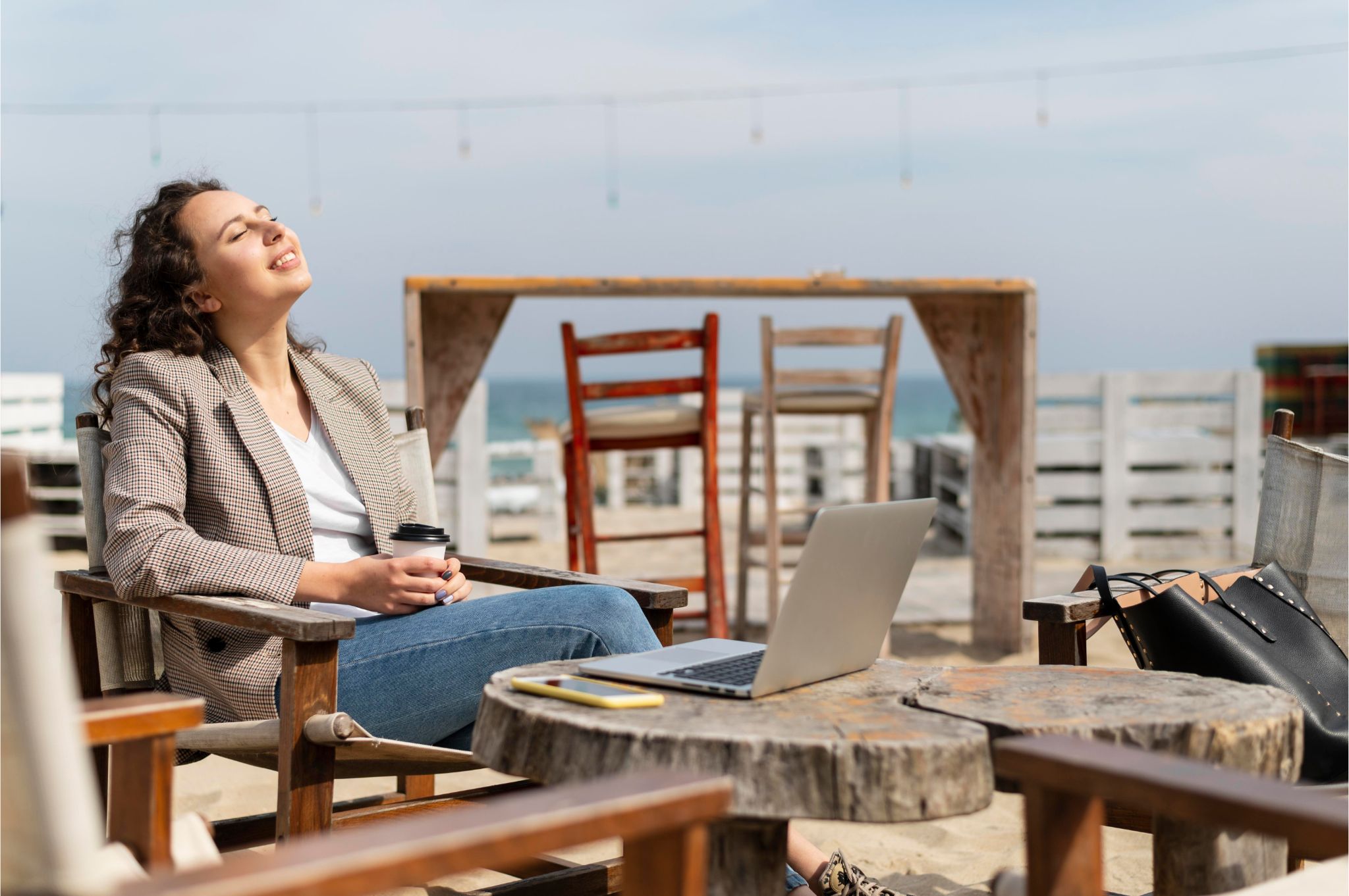 Digital nomad woman relaxing on a beach café with laptop and coffee while working remotely