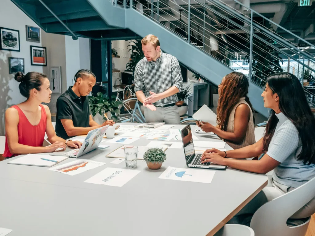 Bright open-plan coworking space with large windows, laptops on wooden desks, and visible power outlets